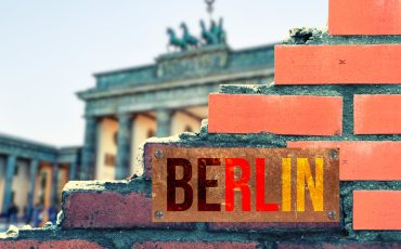 Eine Mauer, ein Blick auf Brandenburger Tor und ein Schild Berlin